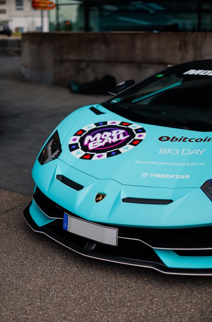 Close-up of a customized turquoise sports car with branding decals in urban setting.